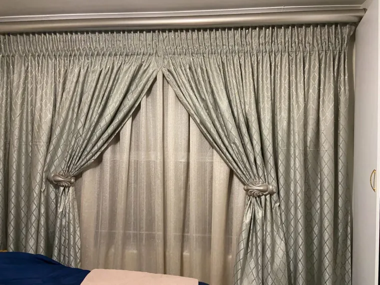 Silver-green pinch-pleat curtains with hold-backs over sheers in a Cape Town bedroom