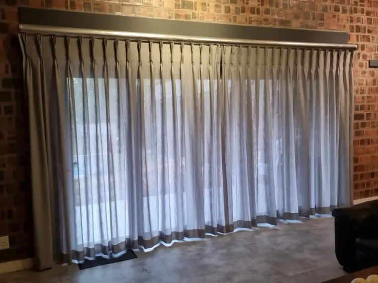 Silver sheer curtains with a dark border in a Cape Town brick-wall lounge