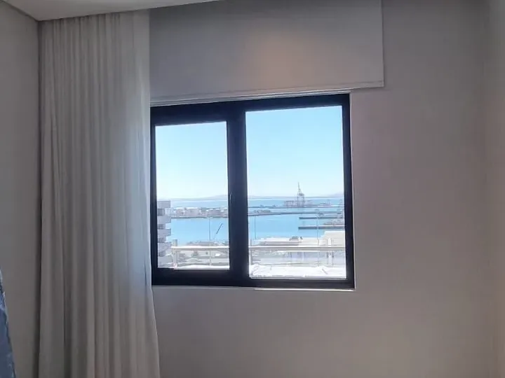 Roller blind raised to show the sea view, with a sheer curtain, in a Strand bedroom, Cape Town